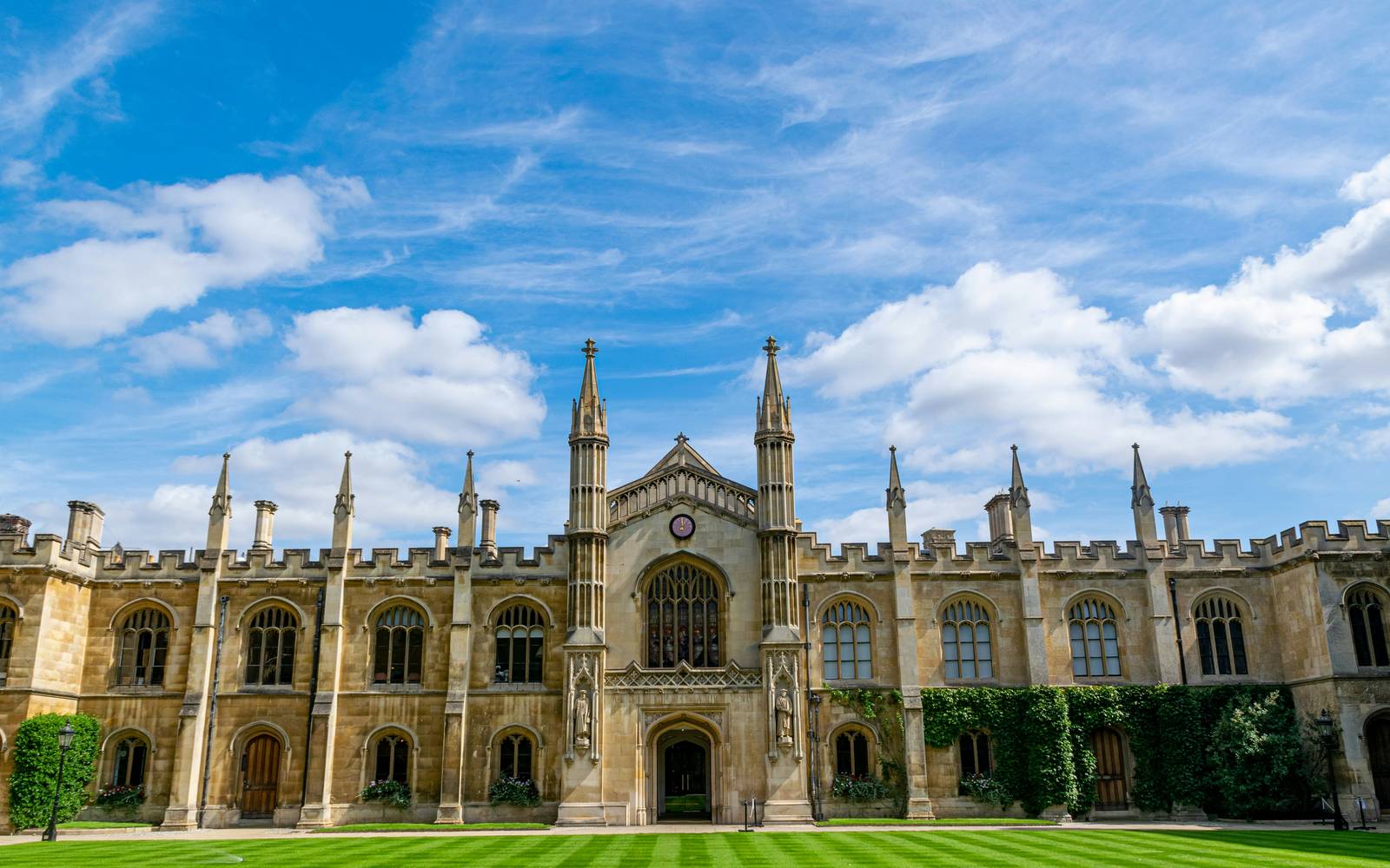 King's College in Cambridge seen from the lawn, with its Gothic facade, pinnacles, central clock and tall arched windows under a blue sky