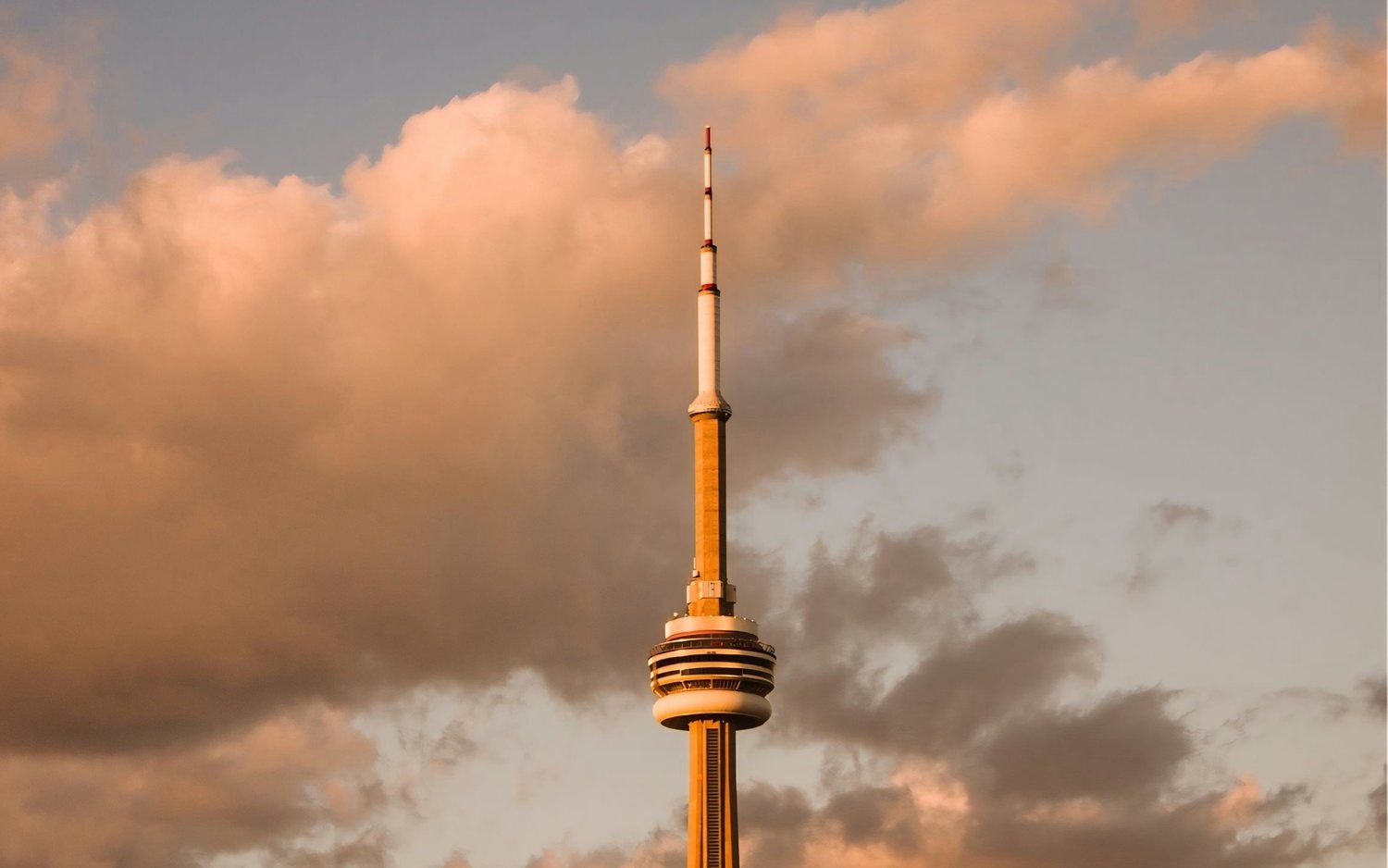 The CN Tower in Toronto at sunset, with its spire and observation pod rising above the city against a warm golden sky